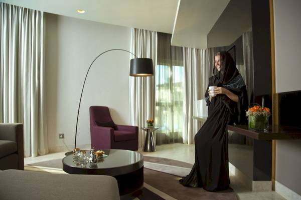 Eine Frau im schwarzen Kleid steht im Hotel Al Ain Rotana und hält einen Kaffee in der Hand.