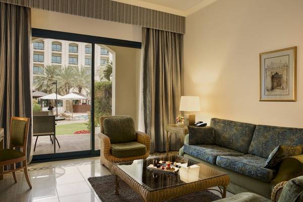 Wohnzimmer des Al Ain Rotana Hotels mit Glastür, Couch, Tisch und Bild an der Wand.