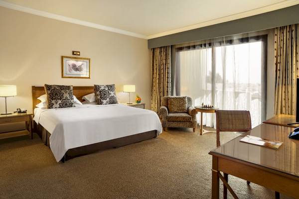 Doppelbett-Hotelzimmer im Al Ain Rotana mit großem Fenster und Sitzbereich.