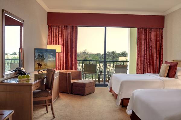 Zimmer im Al Ain Rotana Hotel mit Balkon, Fernseher und Schreibtisch.