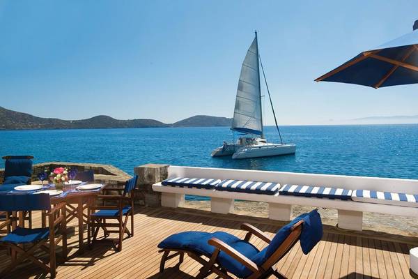 Elounda Beach Hotel & Villas: Terrasse mit Tisch, Stühlen und Boot im Wasser.