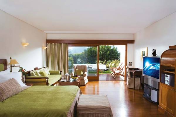 Innenansicht einer Suite im Elounda Beach Hotel & Villas mit großem Bett, Wohnzimmer und Terrassenzugang.