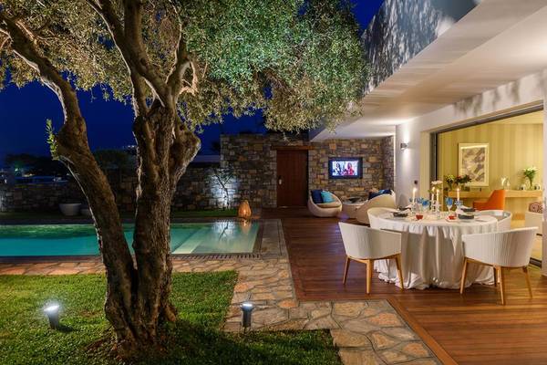 Außenbereich des Elounda Beach Hotel & Villas bei Nacht mit Swimmingpool und Esstisch.