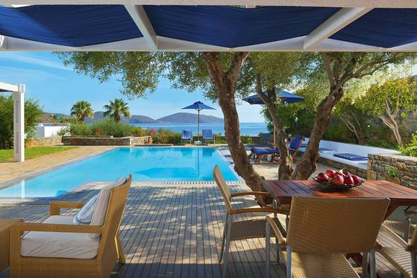 Pool-Terrasse des Elounda Beach Hotel mit Blick auf das Meer und Palmen.