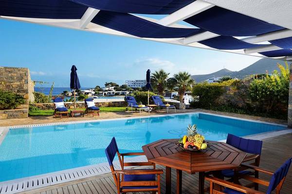 Außenpool des Elounda Beach Hotel & Villas mit Terrasse, Lounge-Stühlen und einem Tisch mit Obst.