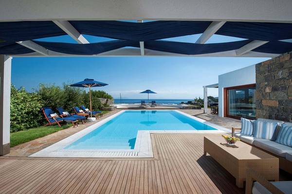 Pool-Terrasse im Elounda Beach Hotel mit Blick auf das Meer und blauen Sonnenschirmen.