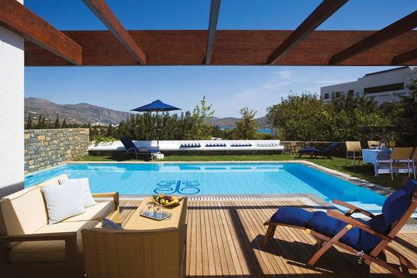 Außenbereich des Elounda Beach Hotel & Villas mit Swimmingpool, Sonnenliegen und Möbeln.