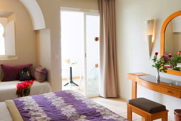 Schlafzimmer im Djerba Resort Hotel mit zwei Betten, Kissen, Nachttisch, Spiegel und Glastisch mit Blumen.