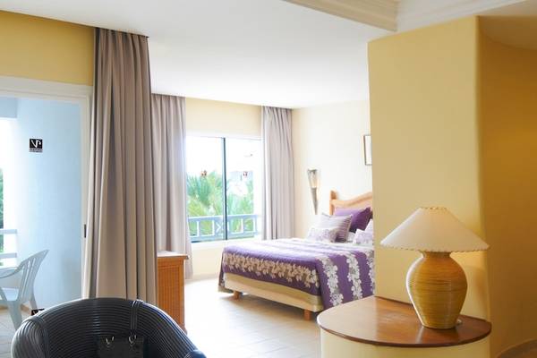 Innenansicht eines Zimmers im Djerba Resort Hotel mit Bett, Tisch und Lampe.