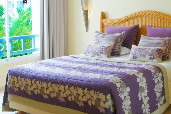Bett im Djerba Resort Zimmer mit violettem Bettzeug und Blumenvase neben dem Bett.