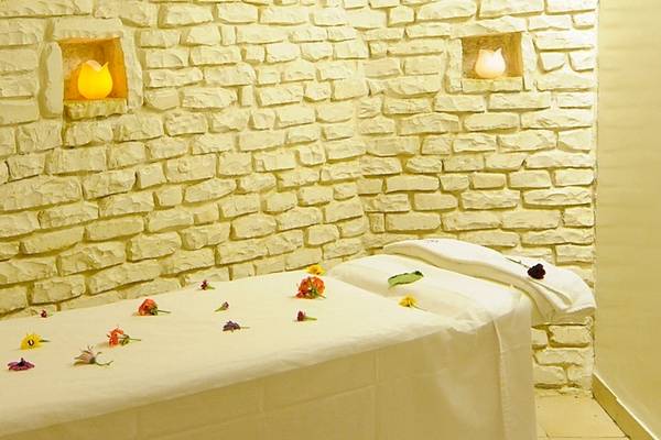 Massageraum im Djerba Resort mit weißen Steinwänden, zwei eingelassenen Kerzen und einem Massagetisch mit Blumen