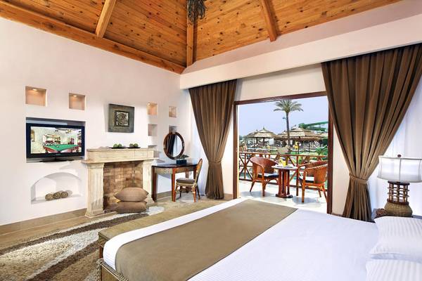 Innenansicht eines Schlafzimmers im Pickalbatros Aqua Blu Resort - Sharm mit Kamin, Fernseher, Tisch und Balkon mit Meerblick.