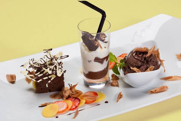 Ein weißer Teller mit einem Brownie, einem Glas mit Schokoladengetränk und Eiscreme sowie einem Eiskübel.