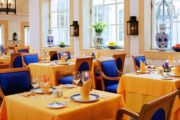 Interieur des Restaurants im Seaside Grand Hotel Residencia mit blauen Stühlen und gelben Tischdecken.