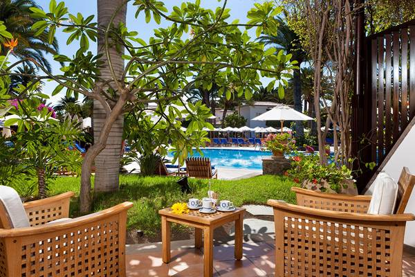 Gartenbereich des Seaside Grand Hotel Residencia mit hölzernen Stühlen und einem Tisch.