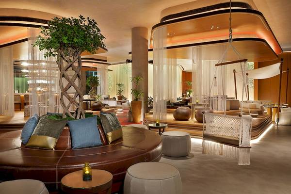 Lobby des W Muscat Hotels mit zentralem Baum, braunem Sofa und Hängesessel.