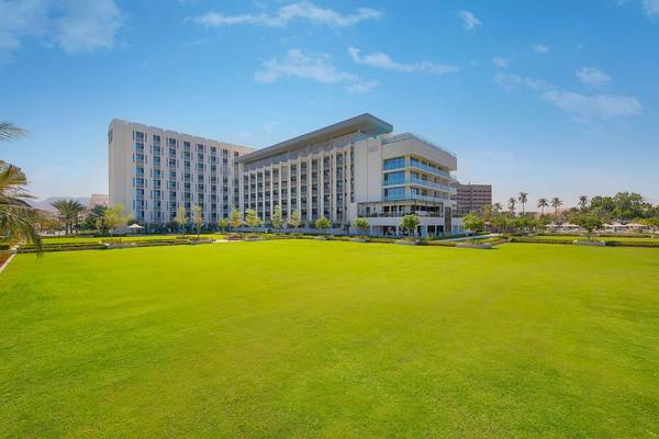 Außenansicht des W Muscat Hotels mit weitläufigem Rasen und moderner Architektur.