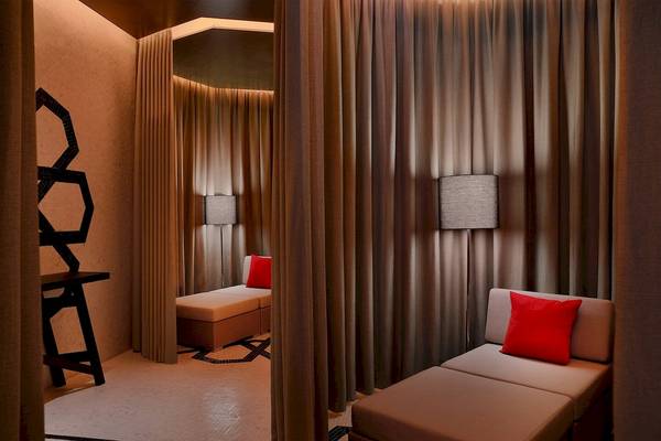 Loungebereich im W Muscat Hotel mit zwei Sesseln, roten Kissen und braunen Vorhängen.