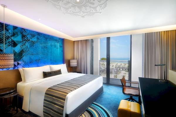 Hotelzimmer im W Muscat mit blauer Wand, Bett, Schreibtisch und Meerblick.