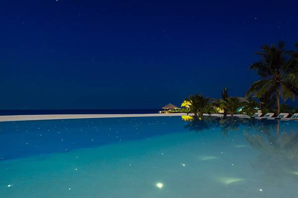 Nachtansicht des beleuchteten Pools im Velassaru Maldives Hotel mit Sternenhimmel und Palmen