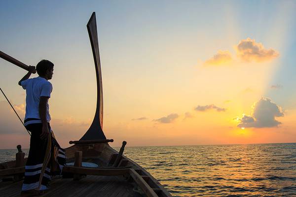 Sonnenuntergang auf See von einem Boot aus gesehen, Person steht am Heck