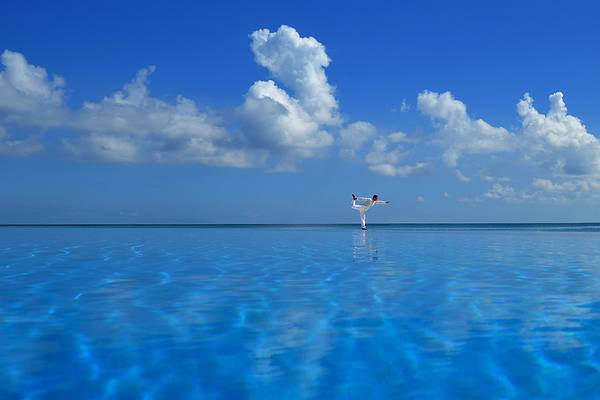 Eine Person praktiziert Yoga in einem kristallklaren Infinity-Pool im Velassaru Maldives.