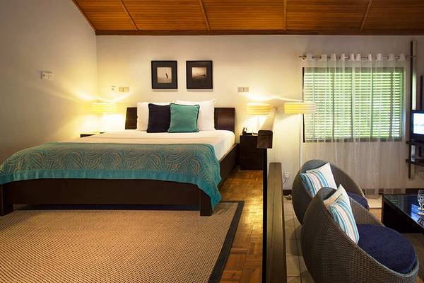 Innenansicht eines Hotelzimmers im Velassaru Maldives mit einem Bett, Fernseher und Wohnzimmerbereich.