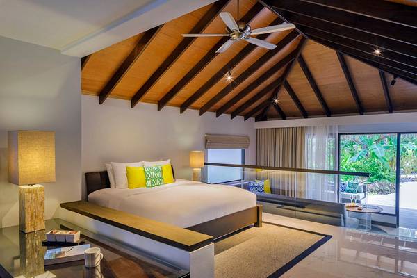Schlafzimmer im Velassaru Maldives Hotel mit Doppelbett, Deckenventilator und Glaswänden.
