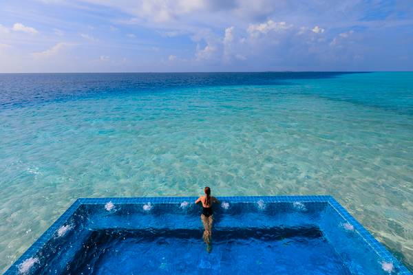 Eine Frau im schwarzen Bikini steht in einem Infinity-Pool des Velassaru Maldives mit Blick auf das Meer.