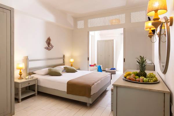 Innenansicht eines Schlafzimmers im Almyrida Beach Hotel mit Bett, Nachttischen und Obstplatte.