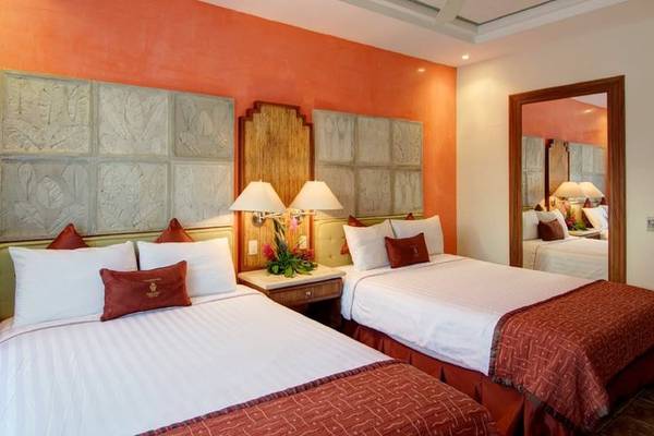 Doppelbettzimmer im Tamarindo Diria Beach Resort mit orangefarbenen Wänden, zwei Betten, Nachttischen und Lampen.