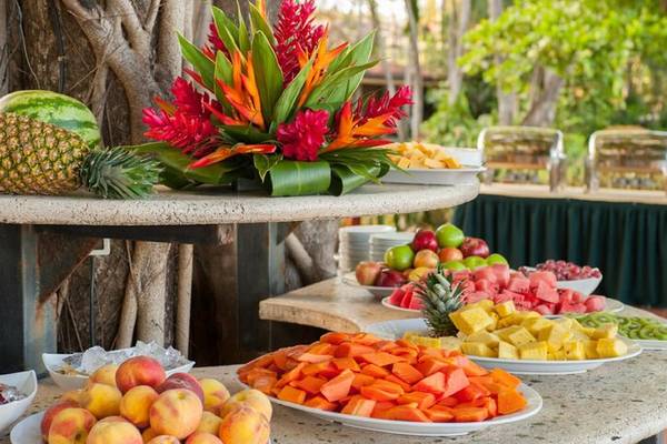 Obstbuffet im Tamarindo Diria Beach Resort mit verschiedenen Früchten und einem Blumenarrangement.