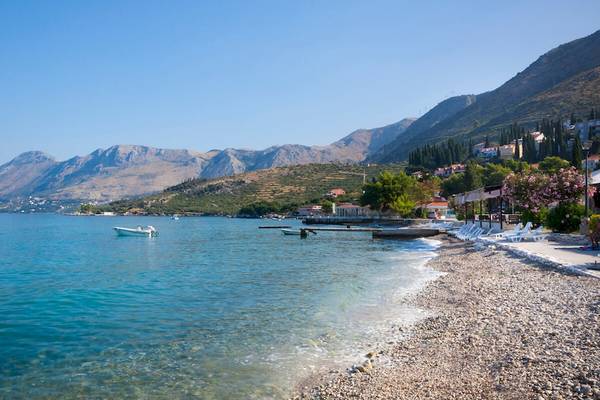 Remisens Hotel Albatros Strand mit Boot und Bergen im Hintergrund