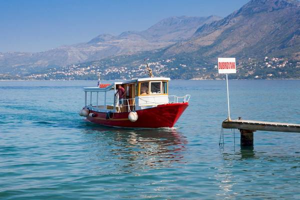 Ein rotes Boot im Wasser vor einem doppelten Anleger mit Bergen im Hintergrund