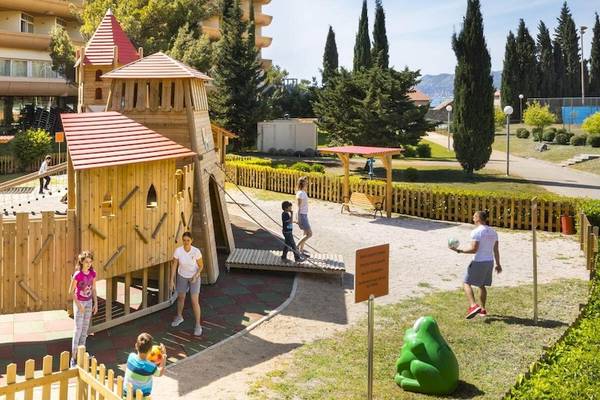 Kinder spielen auf einem großen Holzspielplatz im Freien vor dem Remisens Hotel Albatros.