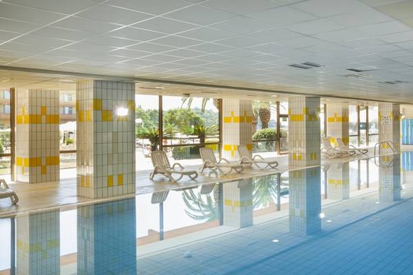 Innenpool des Remisens Hotel Albatros mit gelben und weißen Säulen, blauen Kacheln und leeren Liegestühlen.