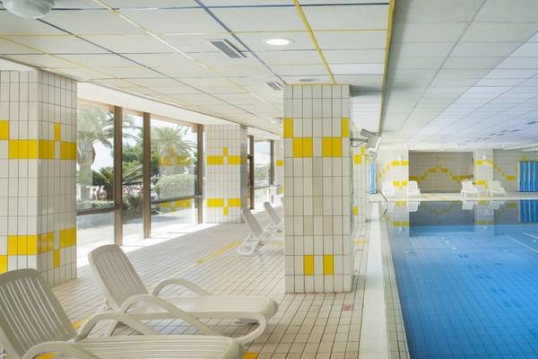 Innenpool des Remisens Hotel Albatros mit weißen und gelben Kacheln, Loungestühlen und blauem Wasser