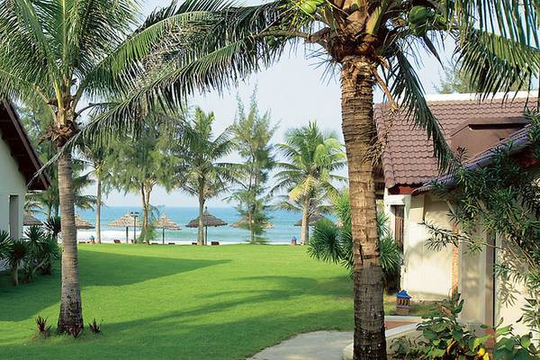 Außenansicht des Palm Garden Beach Resort Hoi An mit Häusern, Palmen und einem Blick auf das Meer.