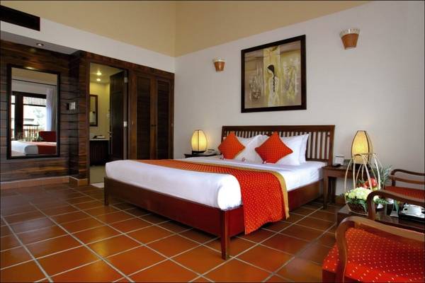 Schlafzimmer im Palm Garden Beach Resort Hoi An mit einem großen Bett, roten Kissen und einem gerahmten Bild an der Wand.