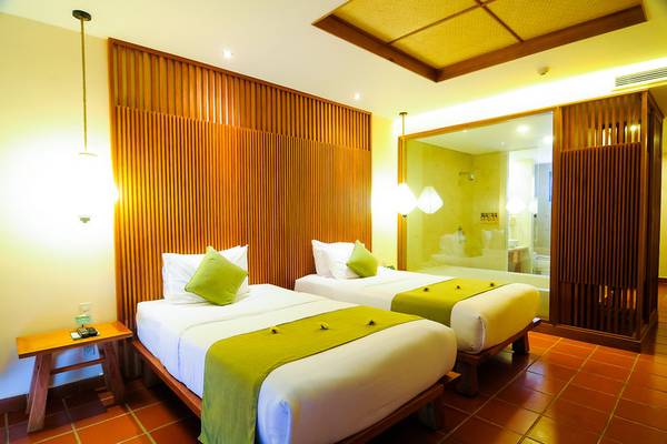 Doppelbett-Zimmer im Palm Garden Beach Resort Hoi An mit zwei Betten, grünen Kissen und braunen Holzwänden.