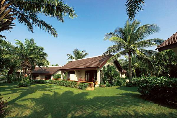 Außenansicht des Palm Garden Beach Resort Hoi An mit braunem Dach und grünem Rasen.