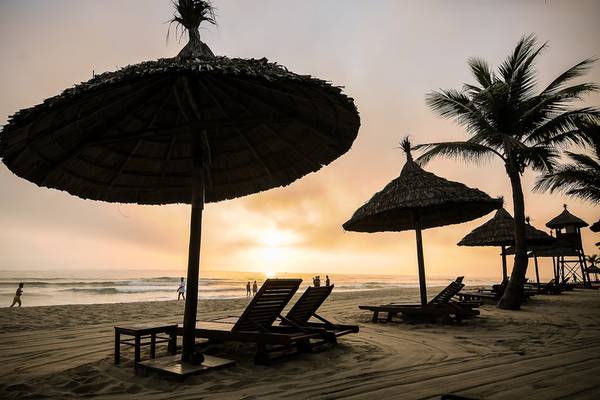 Strand des Palm Garden Beach Resort Hoi An bei Sonnenuntergang mit Sonnenschirmen und Liegen.