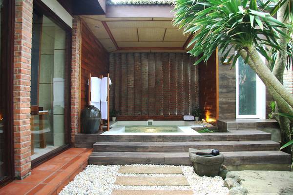 Außenwhirlpool im Palm Garden Beach Resort Hoi An mit Holz- und Ziegelwänden.