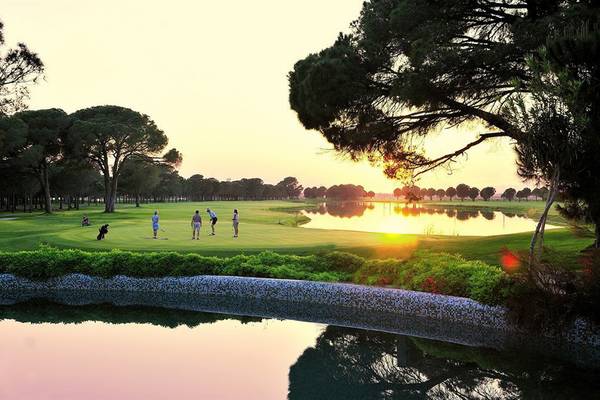 Golfplatz mit Sonnenuntergang im Hintergrund und mehreren Spielern in Aktion.