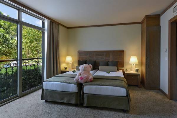 Doppelbett-Zimmer mit Balkon im Gloria Verde Resort mit Blick auf die Bäume und einem Teddybär auf dem Bett.