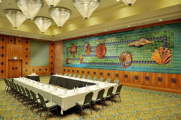 Konferenzraum im Gloria Verde Resort mit großen Tisch, farbigen Wanddekorationen und Kronleuchtern.