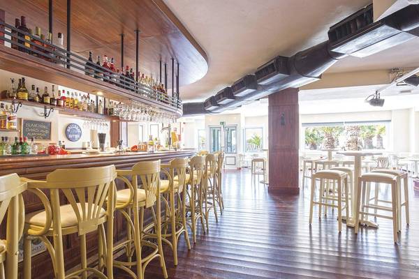 Bar im Be Live Experience Lanzarote Beach Hotel mit gelben Stühlen und einer Theke mit Flaschen.
