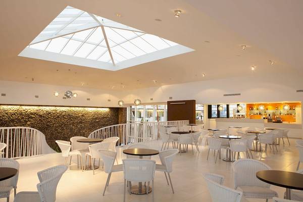 Innenbereich des Be Live Experience Lanzarote Beach Hotels mit vielen Tischen und Stühlen, hoher Glaskuppel und Steinwand.