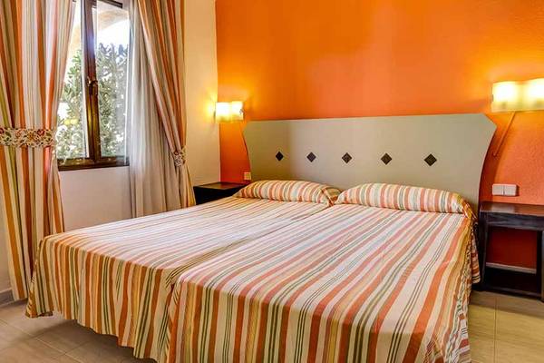 Doppelbett im Hotelzimmer im SBH Taro Beach mit orangefarbenen Wänden und gestreiften Bettdecken.
