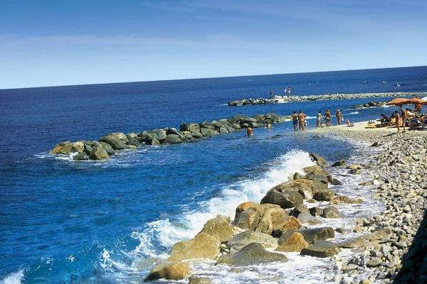 Strand mit Felsen und Meer im Hintergrund, einige Menschen baden und entspannen
